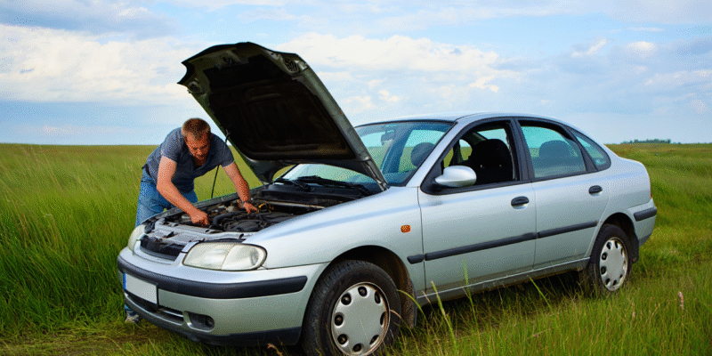 Homme qui essaie de réparer sa voiture en pleine campagne